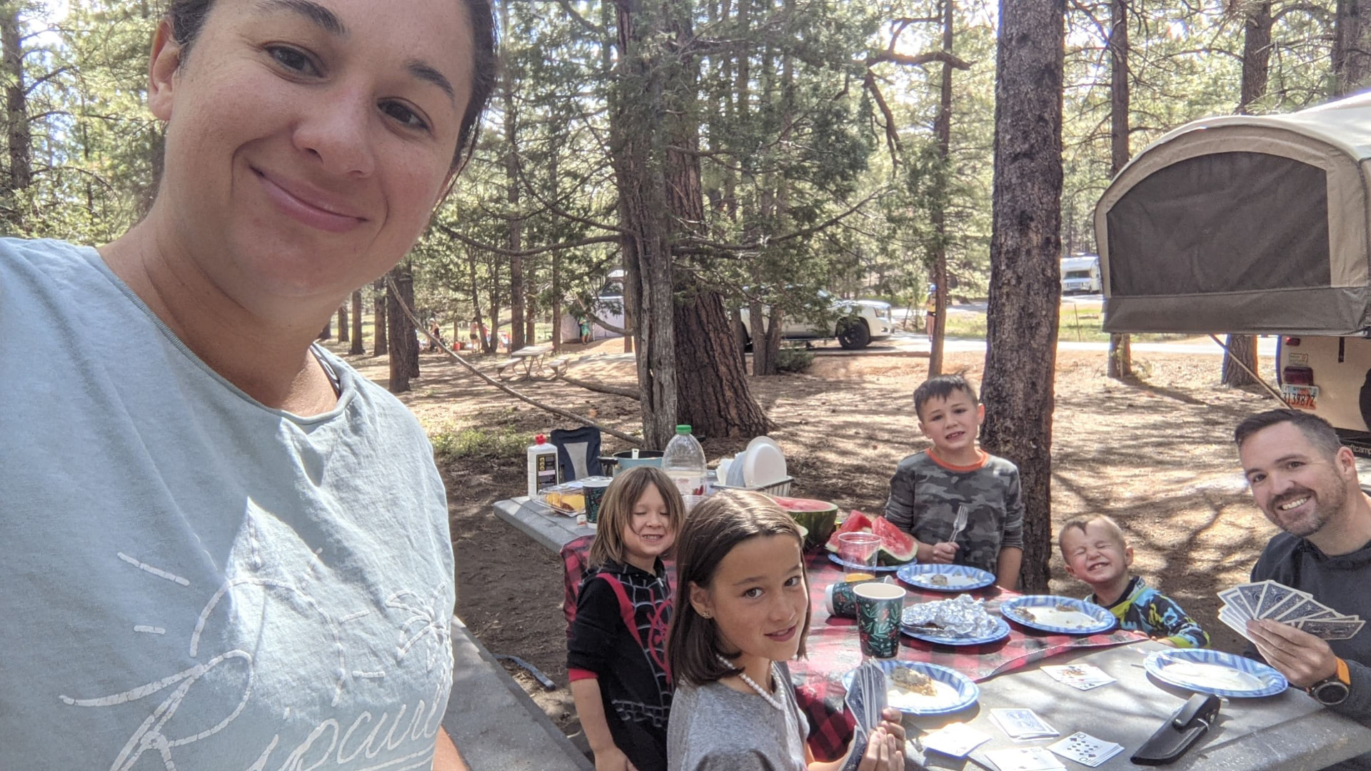 Leah holding the camera for a selfie while the family plays cards at the campsite table