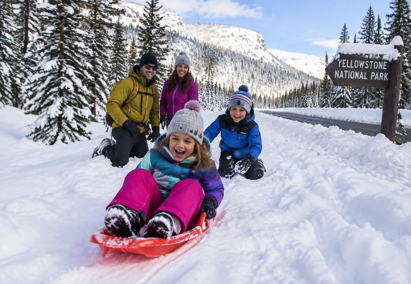 Children in snow gear sledding and playing beside a plowed road in snowy Yellowstone